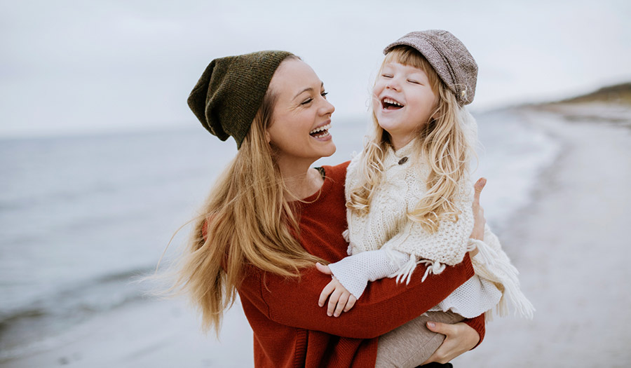 image of a mother holding younger daughter at the beach and smiling for a blog about how to handle mothers day when you have lost your mum