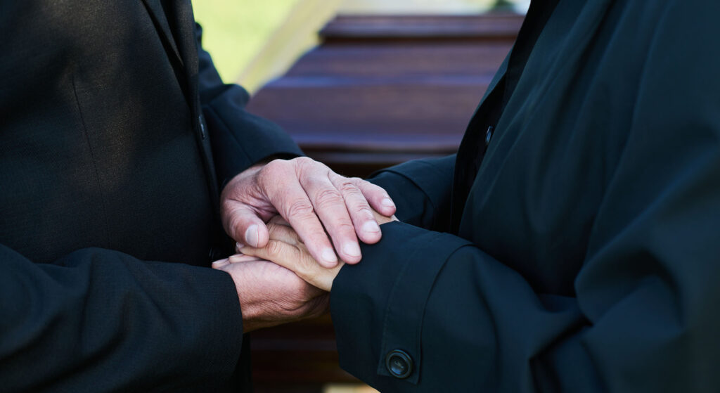 Two people holding hands in front of a coffin.